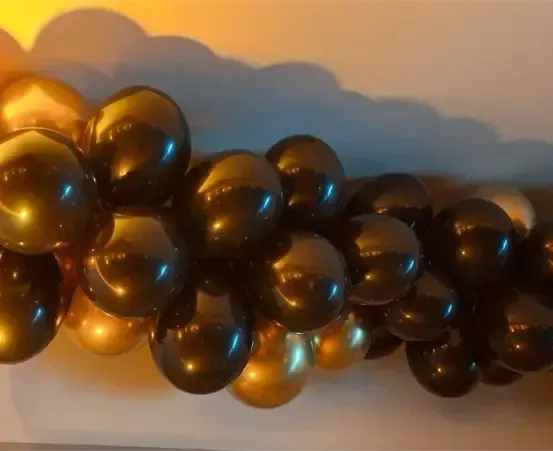 Eine Sammlung schwarzer und goldener Folienballons ist auf einer Oberfläche mit einem blau-weißen Hintergrund gruppiert.