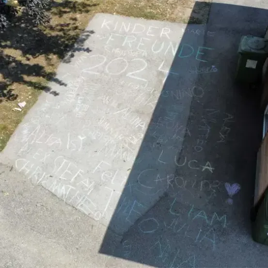 Ein Gehweg mit Kreideinschriften, darunter Namen wie Luca, William und Caroline, wobei einige Buchstaben teilweise gelöscht sind.