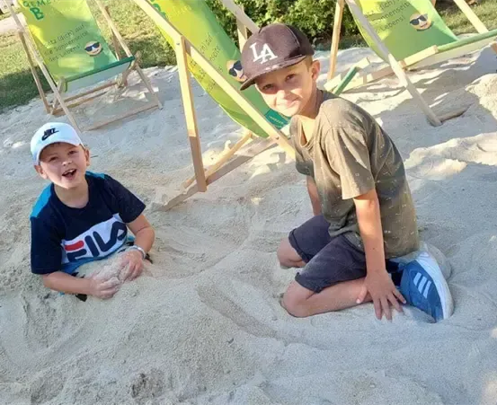 Zwei Kinder spielen am Strand im Sand. Eines trägt ein blaues T-Shirt und das andere ein braunes.