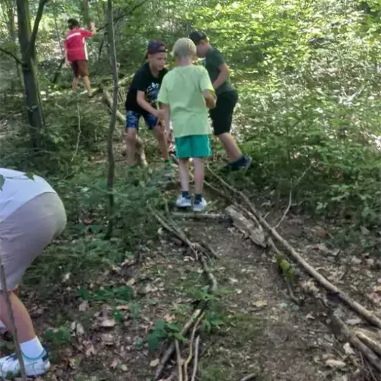 Mehrere Personen wandern im Wald. Eine Person beugt sich hinunter, um etwas aufzuheben. Eine andere Person hält einen Stock.