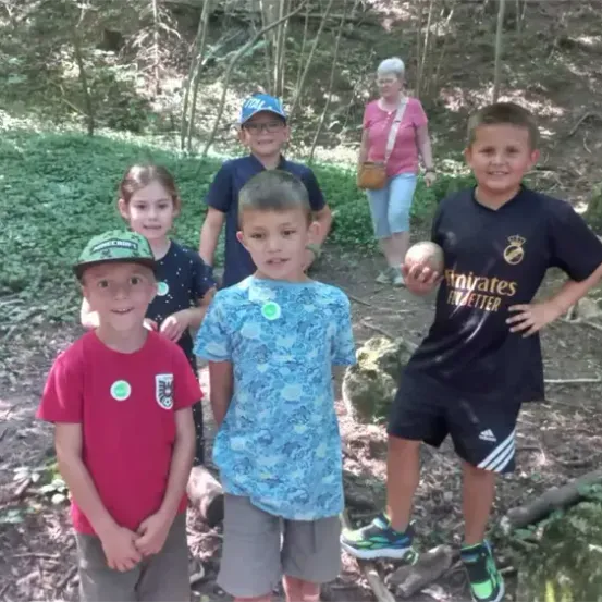 Eine Gruppe von Kindern und eine erwachsene Frau stehen in einem Wald, lächeln und posieren für ein Foto.