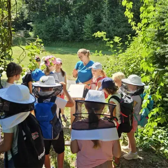 Eine Gruppe von Kindern und einem Erwachsenen in Schutzkleidung befindet sich in einem Garten, möglicherweise lernen sie etwas über Bienen.