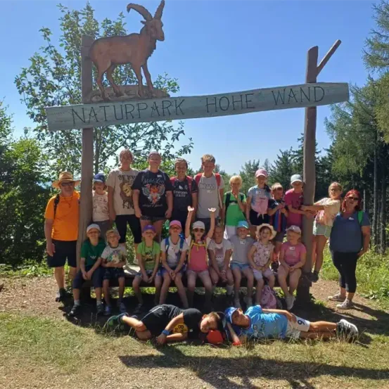 Eine Gruppe von Menschen und Kindern posiert für ein Foto vor einem Schild des Naturparks Hohe Wand.