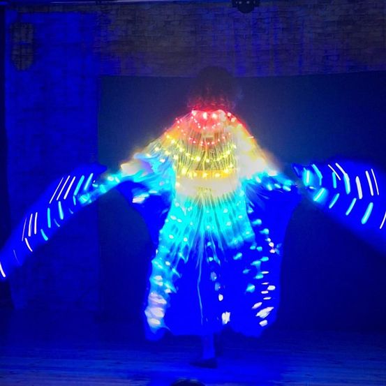 Ein Darsteller auf der Bühne mit einem blauen und mehrfarbigen LED-Kleid, das die dunkle Umgebung mit leuchtenden Lichtern erhellt.