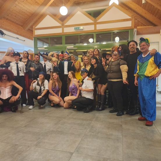 Eine Gruppe von Menschen in Kostümen posiert für ein Foto in einem Raum mit Holzbalken und grünen Türen.