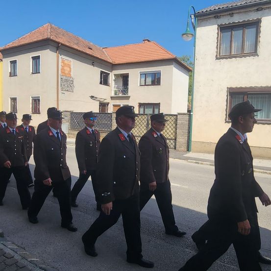 Eine Gruppe uniformierter Männer in Hüten und mit Sonnenbrillen geht unter einem klaren Himmel eine Straße entlang, die von Gebäuden gesäumt ist.