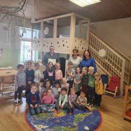 Eine Gruppe von Kindern und Erwachsenen steht und sitzt um eine Weltkarte in einem Spielzimmer herum und posiert für ein Foto.