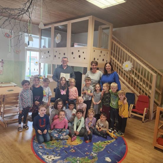 Eine Gruppe von Kindern und Erwachsenen steht und sitzt um eine Weltkarte in einem Spielzimmer herum und posiert für ein Foto.