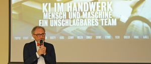 Ein Mann hält eine Rede auf der Bühne vor einem Beamer mit einer Präsentation über Teamarbeit.