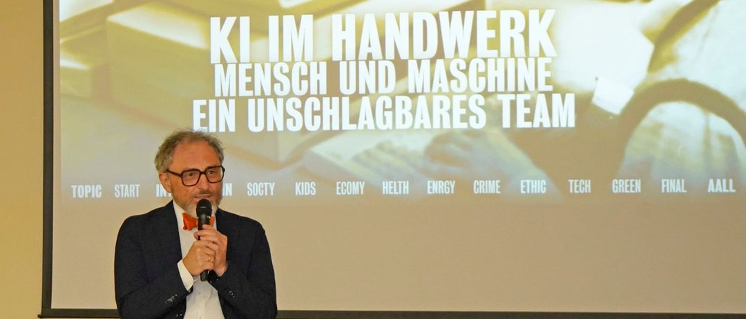Ein Mann hält eine Rede auf der Bühne vor einem Beamer mit einer Präsentation über Teamarbeit.