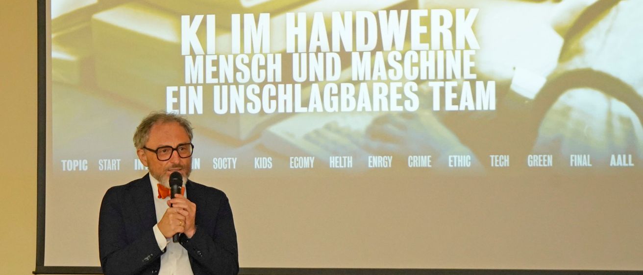 Ein Mann hält eine Rede auf der Bühne vor einem Beamer mit einer Präsentation über Teamarbeit.