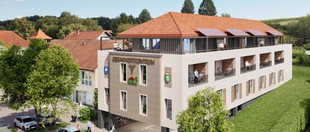 Ein Luftbild eines Gebäudekomplexes mit Solarpanels auf dem Dach. Es gibt Menschen auf den Balkonen und andere, die auf dem Parkplatz spazieren. Autos sind davor geparkt.