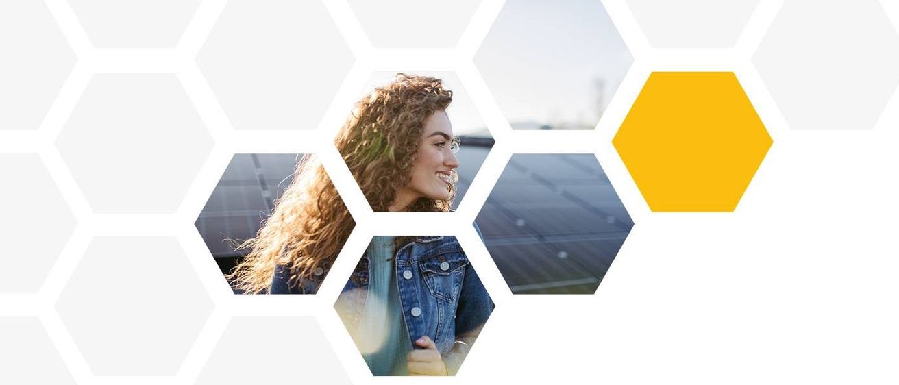 Eine lächelnde Frau mit lockigem Haar steht neben einem sechseckigen Solarpanel, mit einem verschwommenen Hintergrund einer Stadtsilhouette.