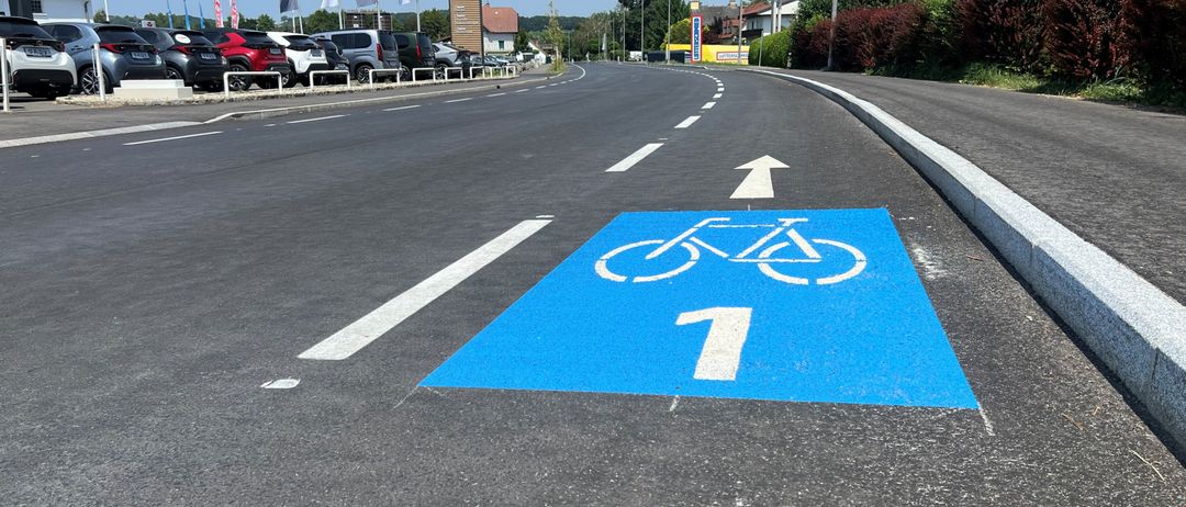 Eine blaue Fahrradspur mit einem Nummer-1-Schild auf einer Straße mit geparkten Autos und Flaggen im Hintergrund.