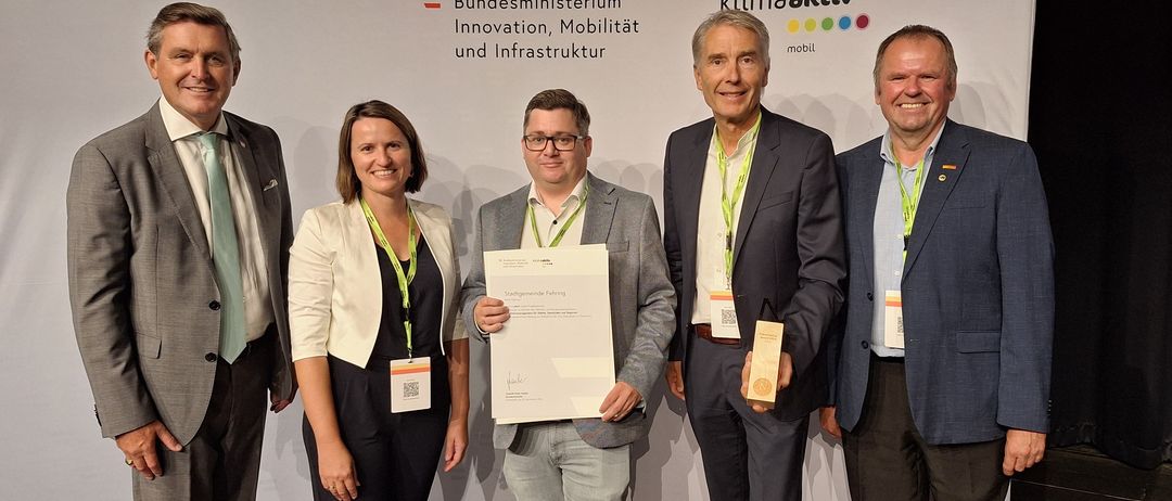 Vier Personen stehen bei einer Preisverleihung zusammen, einer Mann hält ein Zertifikat und ein anderer einen Pokal. Sie tragen alle Namensschilder.