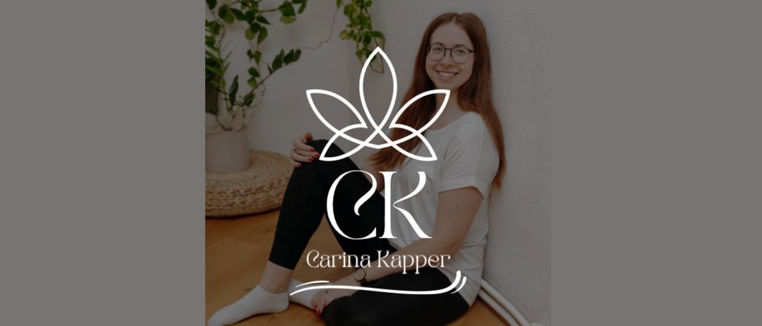 Eine lächelnde Frau sitzt mit überkreuzten Beinen auf dem Boden und trägt ein weißes T-Shirt mit dem Logo von 'CK Carina Kapper'. Sie sitzt neben einer Pflanze in einem weißen Topf.