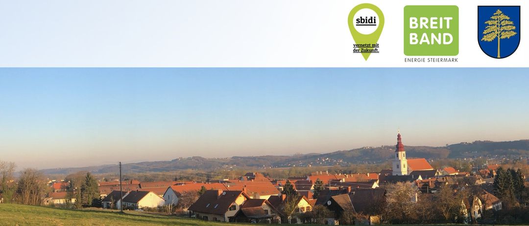 Ein Grasfeld mit einer Stadt im Hintergrund, mit Häusern mit roten Dächern. Ein blaues Schild mit der Aufschrift 'rausbau für Fehring'. Ein kleines grünes Kartensymbol in der oberen rechten Ecke.