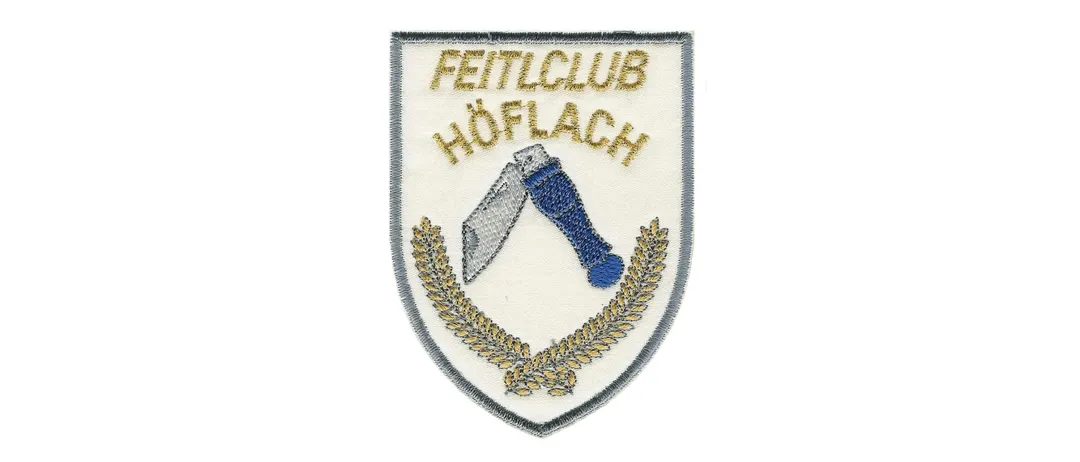 Ein gesticktes Abzeichen mit dem Text 'Fettlclub Hoflach', darunter ein blaues Messer und ein goldener Kranz.