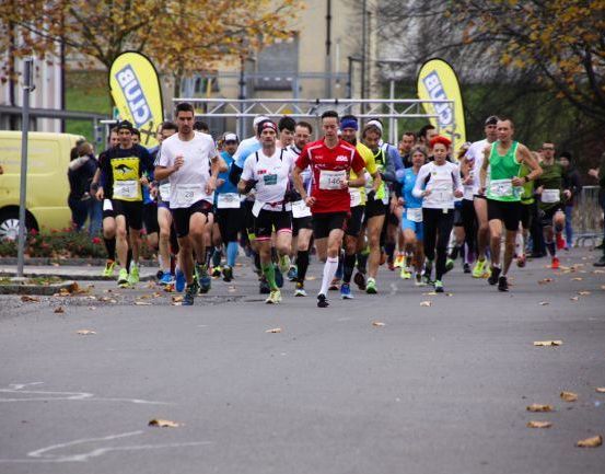 Marathonteilnehmer laufen auf einer asphaltierten Straße mit Bäumen und Gebäuden im Hintergrund.