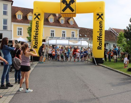 Eine Menschenmenge versammelt sich um einen gelben Bogen mit dem Wort Raiffeisen für eine Laufveranstaltung.