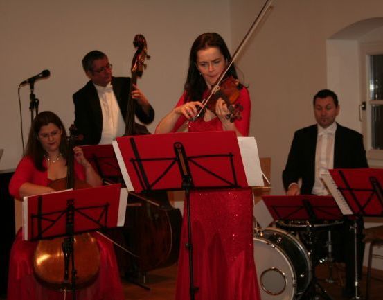 Eine Gruppe von Musikern in roten Kleidern spielt Instrumente in einem Raum mit Mikrofon, Trommel und Fenster.