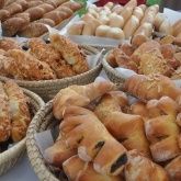 Ein Tisch mit mehreren Körben, die mit einer Vielzahl von Backwaren gefüllt sind, darunter Brötchen, Croissants und Gebäck, in einer Bäckerei präsentiert.