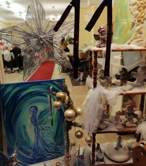 Eine Weihnachtsdekoration mit einem großen silbernen Stern, Figuren und Ornamenten. Ein Gemälde einer Frau mit Flügeln, einem roten Teppich und Stühlen ist ebenfalls zu sehen.