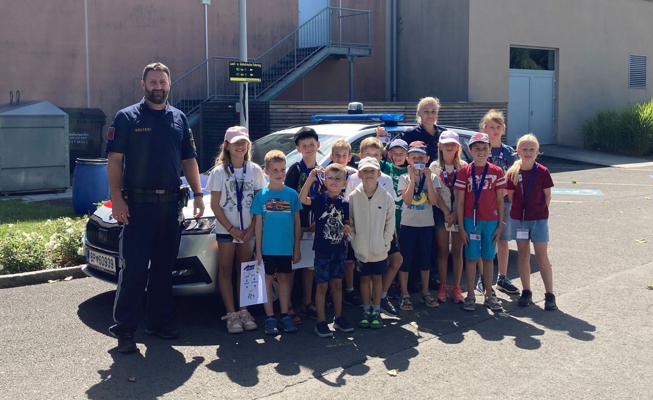 Eine Gruppe von Kindern mit Medaillen um den Hals posiert mit einem Polizeibeamten vor einem Polizeiauto.