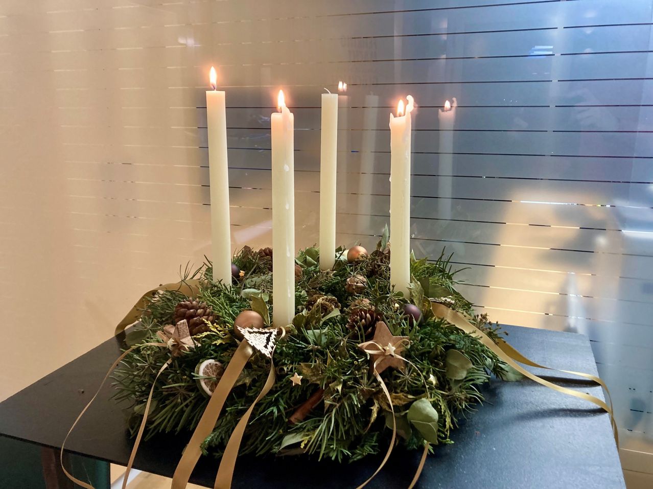 Ein Kranz mit vier brennenden Kerzen und einer Sterndekoration auf einem Tisch mit Tannenzapfen und Blättern.