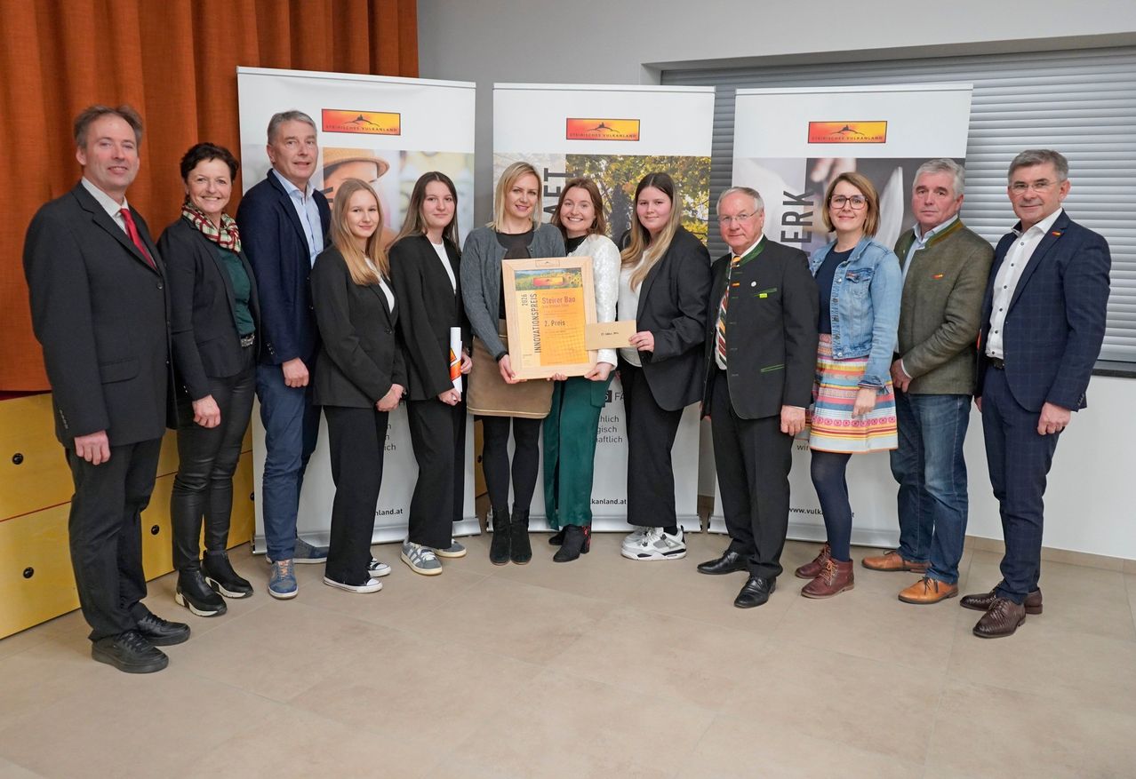 Gruppe von Menschen, die in einer Reihe stehen, zwei halten ein Zertifikat in der Hand und lächeln für ein Foto in einem Konferenzraum.