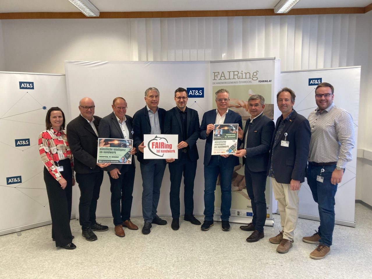 Eine Gruppe von Männern und Frauen steht und hält Urkunden und Banner. Dahinter ist ein Banner mit dem Text FAIRing und AT&S.