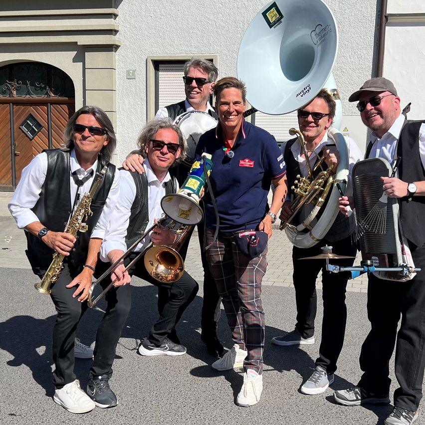 Eine Gruppe von Musikern in Freizeitkleidung posiert mit ihren Instrumenten im Freien für ein Foto.