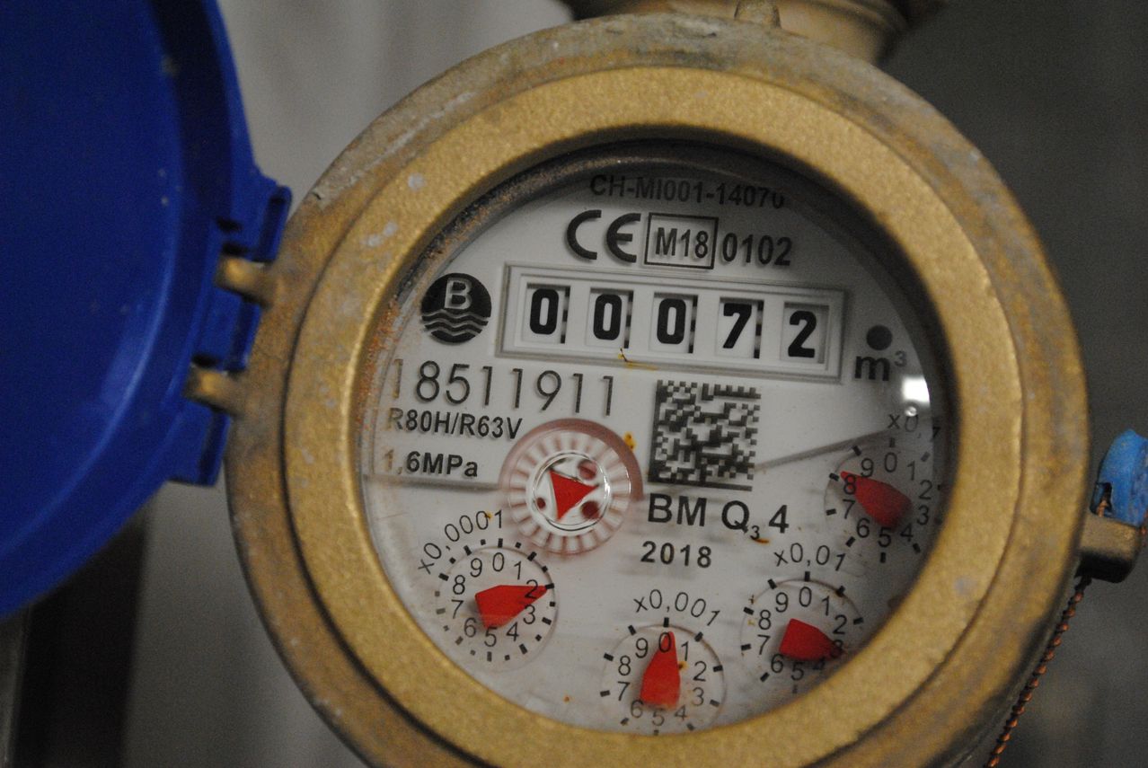 Wasserzähler mit digitalem Display, das 00072 anzeigt. Der Zähler ist CE-zertifiziert, Modellnummer M180102, und hat einen QR-Code. Der Messkopf hat ein rotes Dreieck und drei rote Zeiger.