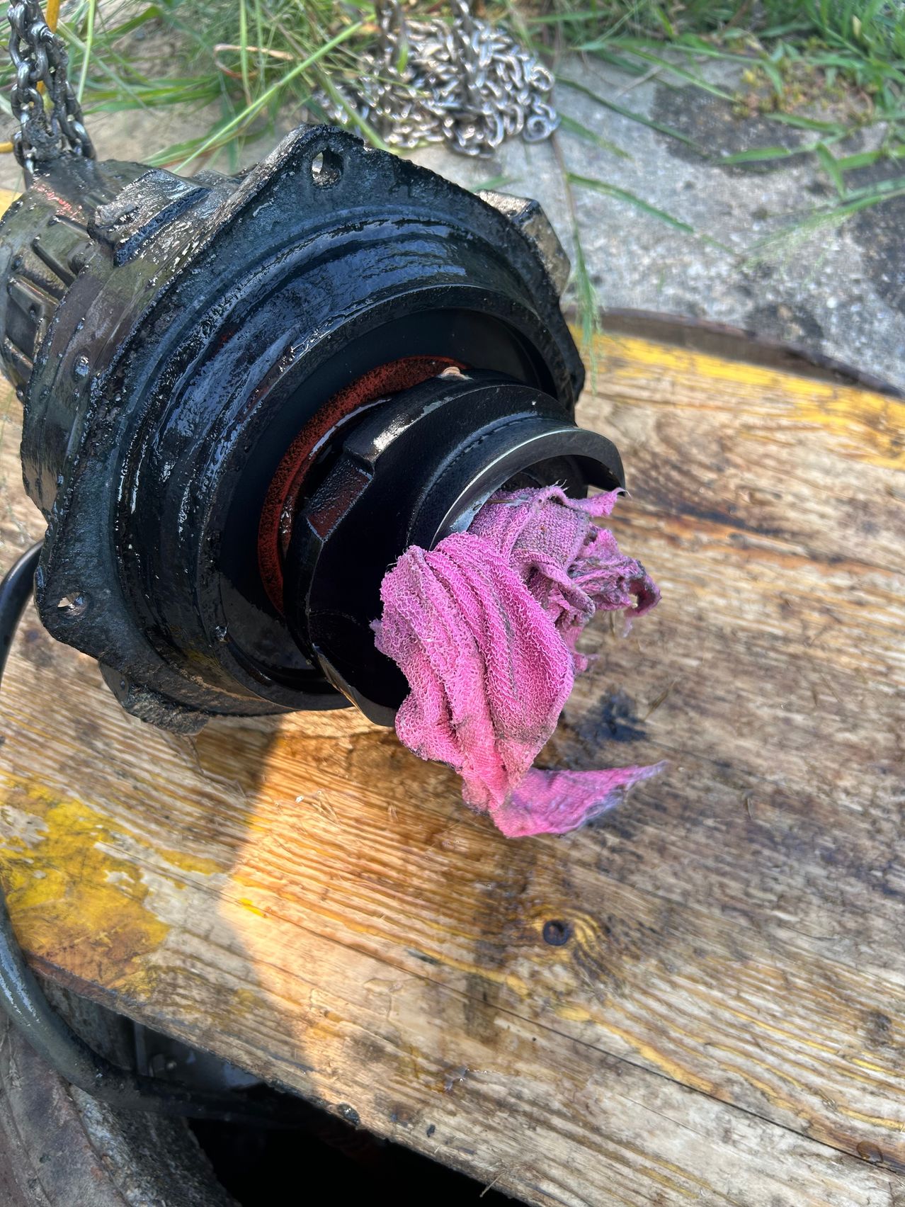 A close-up view of a mechanical part covered in grime, with a pink cloth nearby on a wooden surface.