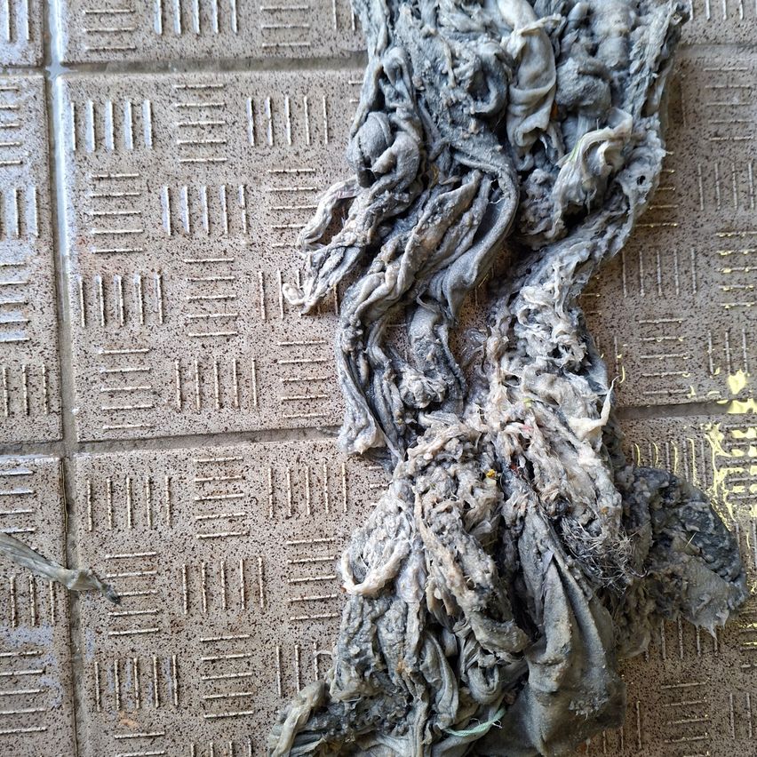 A tangled mass of grey fabric lies on a textured tile floor. The fabric appears to be old and worn, with visible dirt and stains.
