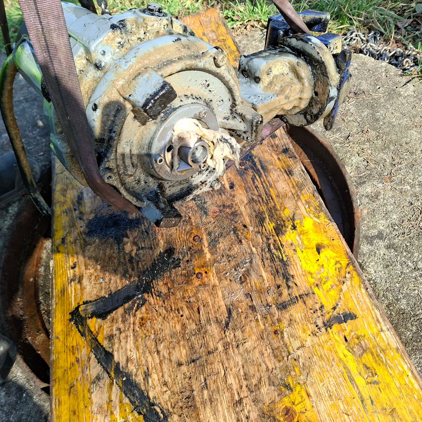 A close-up of a rusty mechanical part, possibly a gear or pump, with yellow and black paint on a wooden plank.