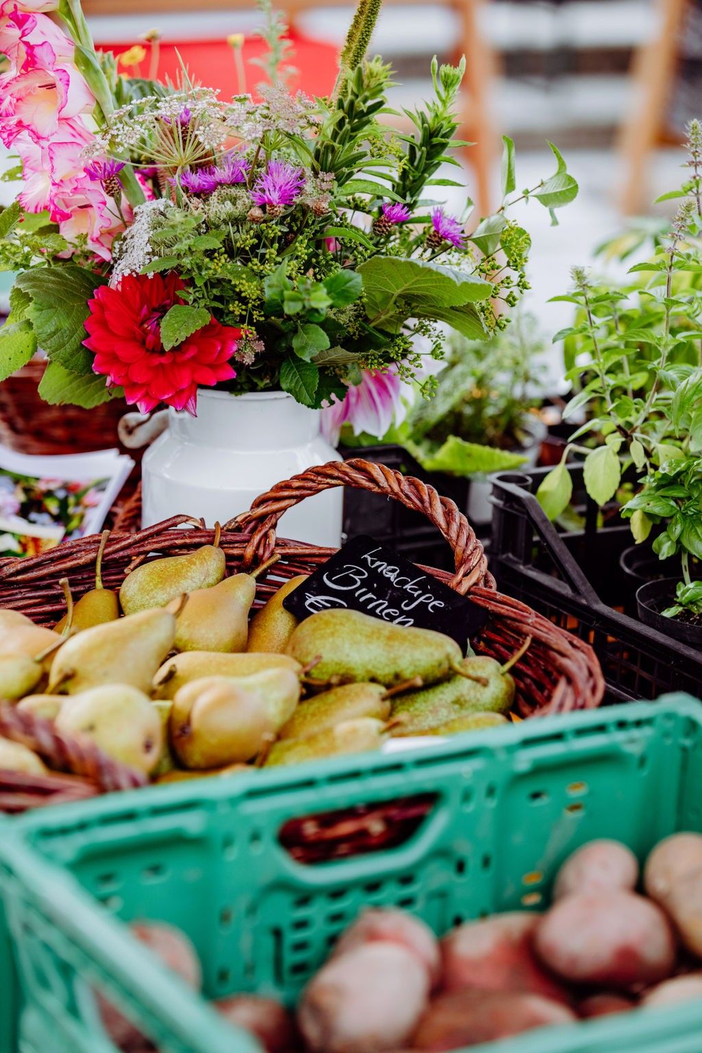 A basket of pears with a label reading 'Knackige Birnen' is displayed next to a vase of flowers.