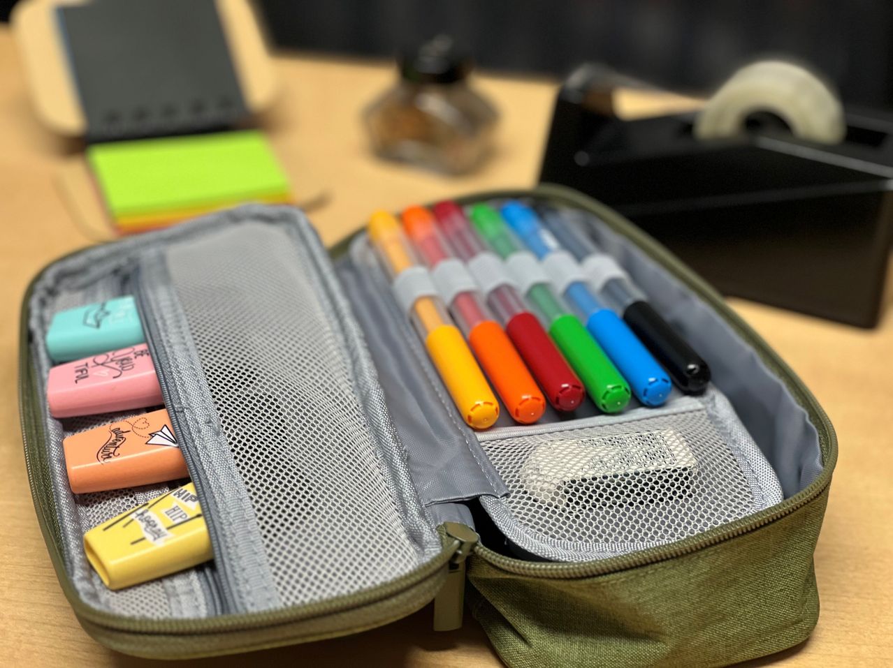 A close-up of a green pencil case with various colored pens and markers inside.