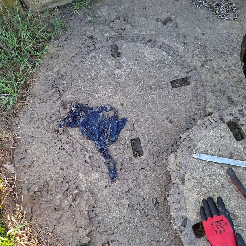 A torn blue piece of fabric lies on a dirty concrete surface near a manhole cover. A red and black glove is nearby.