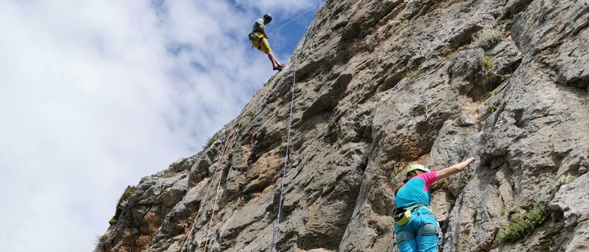 Zwei Kletterer erklimmen eine steile Felswand. Einer ist höher oben auf dem Fels und der andere, in blauer Kletterkleidung und Helm, ist weiter unten.