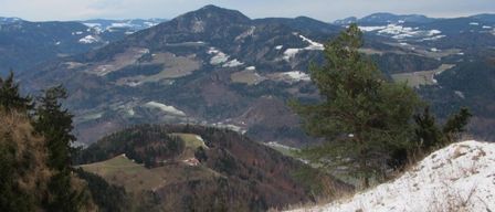 Ein Panoramablick auf eine verschneite Landschaft mit Bergen und einem Haus in der Ferne. Der Himmel ist bewölkt.