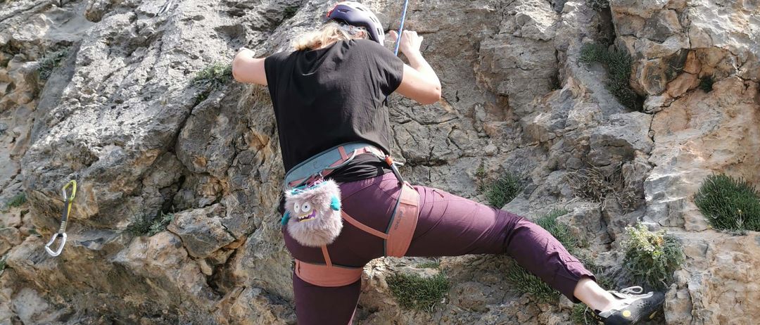 Eine Frau klettert einen steilen felsigen Felsen hinauf, trägt einen Helm und einen Gurt und greift einen Seil für Unterstützung.