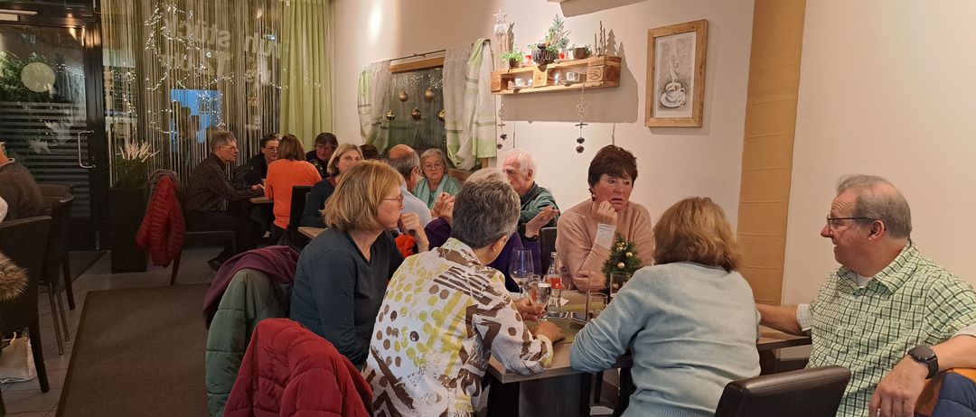 Eine Gruppe älterer Frauen und Männer sitzt in einem Restaurant um einen Tisch herum, mit einem Weihnachtsbaum in der Ecke.