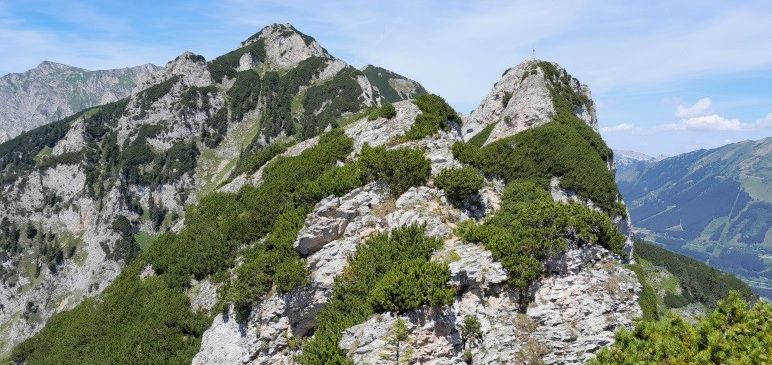 Ein hochgelegener Blick auf raue Berge mit felsigen Klippen und üppigem grünem Bewuchs unter einem klaren blauen Himmel.