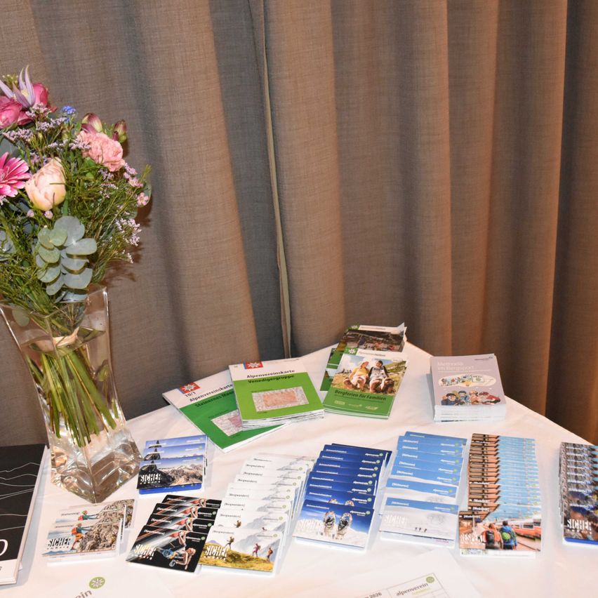 Ein Tisch mit Broschüren und einer Vase mit Blumen, vor dem Hintergrund brauner Vorhänge.