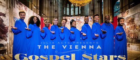 Gruppenfoto eines Chors in blauen Roben, der vor einem Banner mit der Aufschrift 'Julia Acts präsentiert The Vienna Gospel Stars' posiert. Dahinter ist ein großer Kirchenhintergrund zu sehen.