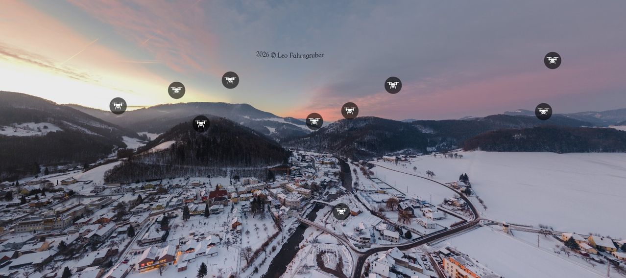 Luftaufnahme eines verschneiten Dorfes mit Bergen im Hintergrund. Das Bild zeigt mehrere Drohnen im Flug.