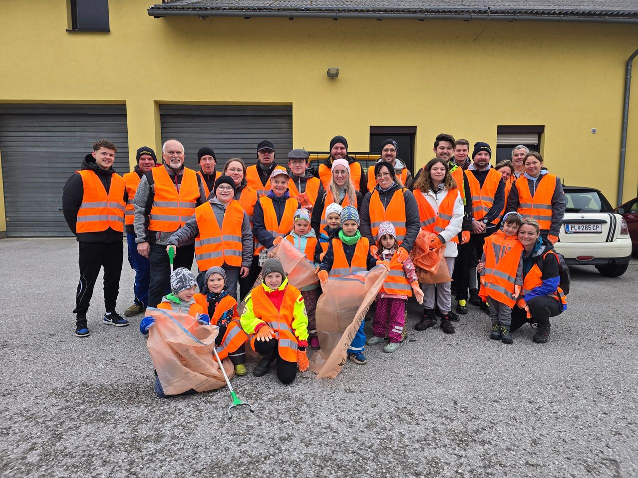 Eine Gruppe von Menschen in orangefarbenen Westen, die Taschen und Stöcke halten, steht vor einem gelben Gebäude und nimmt wahrscheinlich an einer Reinigungsaktion teil.