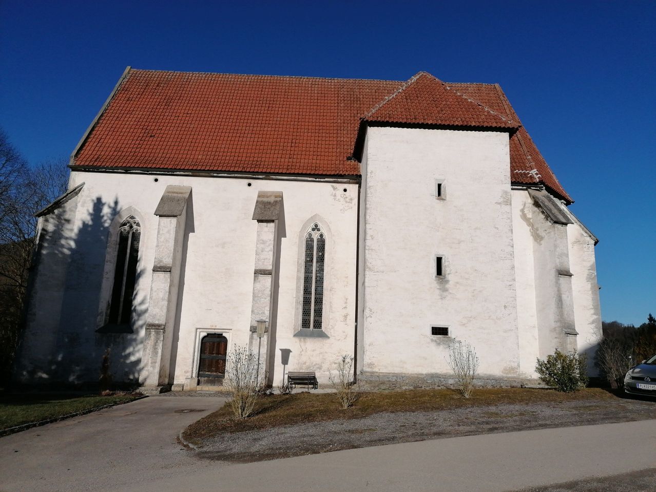 Eine alte weiße Kirche mit einem roten Dach und Bogenfenstern, vor einem klaren blauen Himmel.