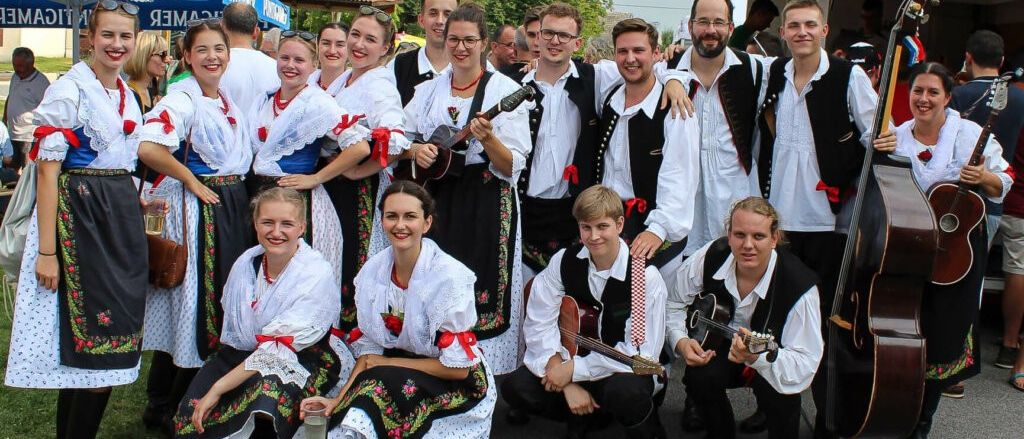 Eine Gruppe von Menschen in traditionellen Kostümen posiert für ein Foto, einige halten Gitarren und lächeln in die Kamera.